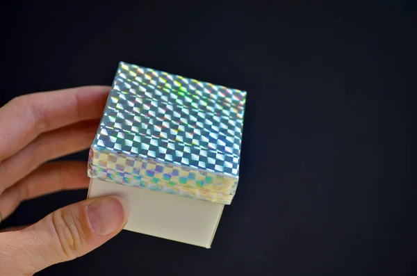 Gift box with rainbow lid in female hand on black background. DIY idea how to decorate a gift with a colored tape