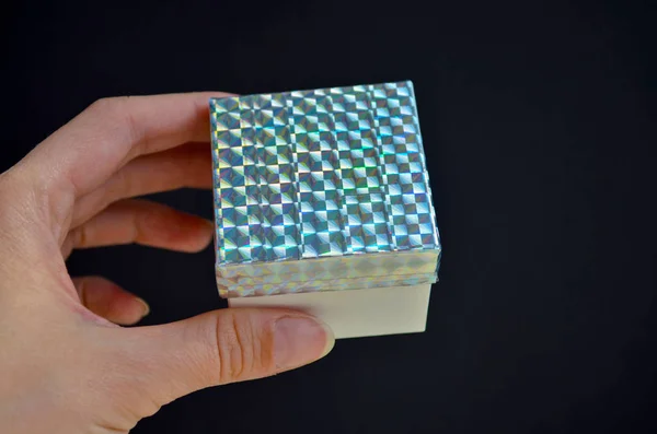 Gift box with a rainbow lid in female hand on black background. DIY idea how to decorate a gift with a colored tape