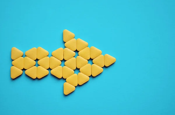 Yellow triangular unusual pills stacked in form of arrow to the right, lie on blue background with copyspace, closeup — 스톡 사진
