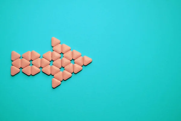 Comprimidos incomuns triangulares rosa empilhados em forma de seta para a direita, deite-se no fundo azul com copyspace — Fotografia de Stock