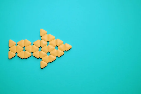 Yellow triangular unusual pills stacked in form of arrow to the right, lie on blue background with copyspace — 스톡 사진