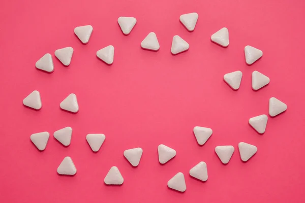 White triangular unusual pills are scattered in the shape of an oval on a pink background with copyspace — 스톡 사진