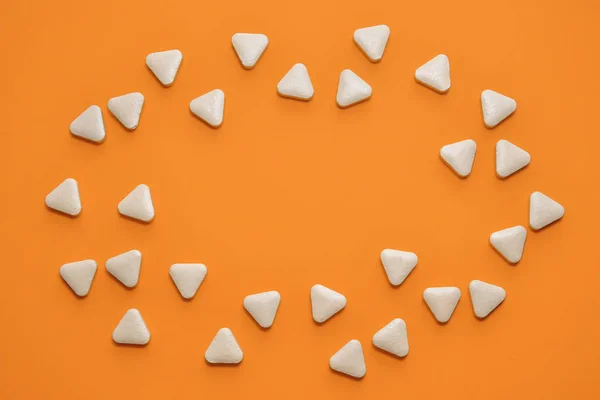 White triangular unusual pills are scattered in the shape of an oval on orange background with copyspace — 스톡 사진