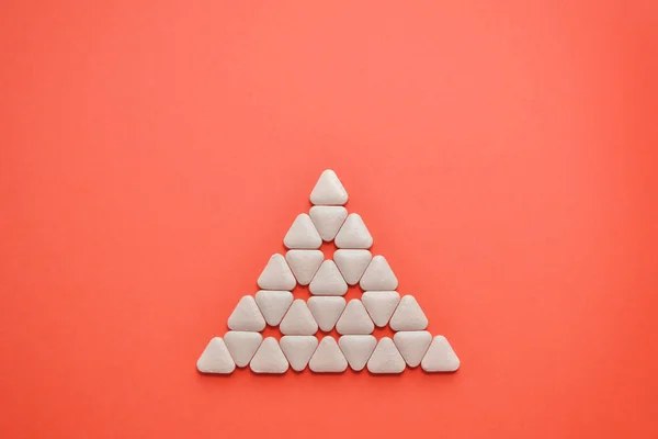 White triangular unusual tablets are laid in the shape of a triangle on a coral background with copyspace — 스톡 사진