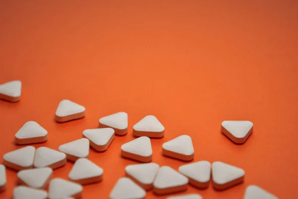 White triangular unusual pills dispersed on a orange background with copyspace — 스톡 사진