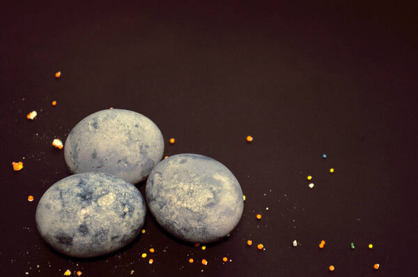 Three eggs, painted hibiscus tea on a black background, in crumbs of sugar glaze, like a dragon egg with copyspace