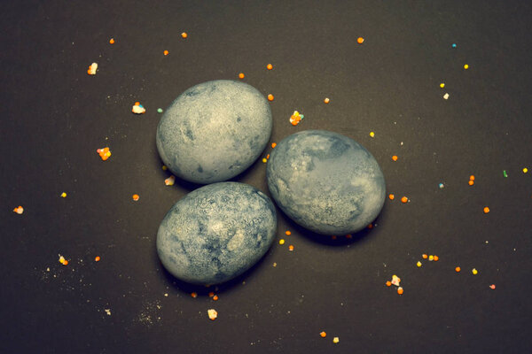 Three eggs, painted hibiscus tea on a black background, in crumbs of sugar glaze, like a dragon egg in blue colors