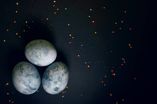 Three eggs, painted hibiscus tea on a black background, in crumbs of glaze, like a dragon egg with copyspace