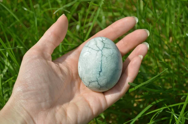 Голубое яйцо с трещиной, окрашенное в чай гибискус, лежит в женской ладони на фоне травы, как драконьи яйца и мрамор — стоковое фото