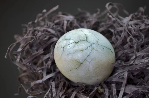 Серые яйца с трещиной, окрашенные в чай гибискус, лежат на бумаге, как гнездо сена на черном фоне крупным планом — стоковое фото