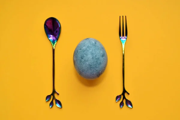 Blaues Ei mit Regenbogengabel und Löffel, bemalt in Tee-Hibiskus, auf gelbem Hintergrund, ähnlich wie Marmor mit Kopierraum — Stockfoto