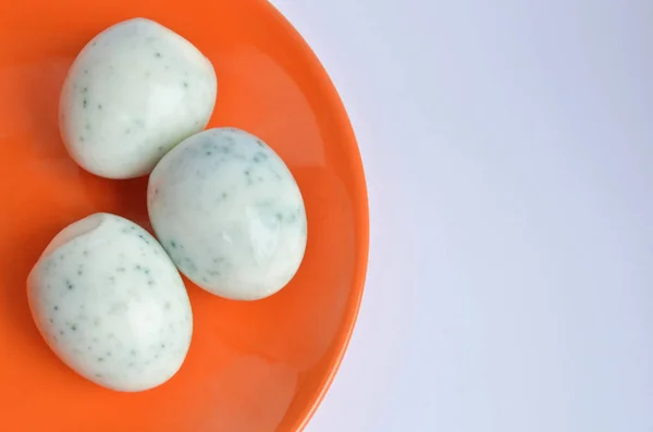 Три очищені яйця після фарбування в чаї з гібіскусом, виглядають як зіпсовані та покриті цвіллю на помаранчевій тарілці з копіспасом — стокове фото