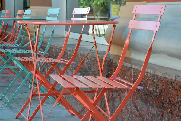 Summer furniture made of metal near cafe. Blue and coral metal tables and chairs closeup