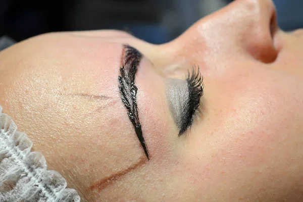 Meisje met make-up liggend in de steriele pet op de procedure van microblading met een afgewerkte wenkbrauw — Stockfoto