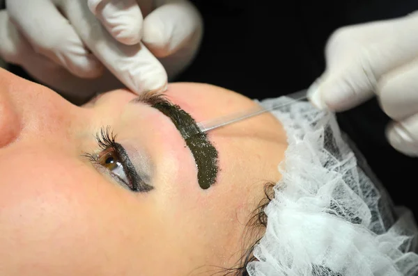 Meisje met make-up liggend op de procedure van microblading. Schoonheidsspecialist maakt permanente make-up op de wenkbrauwen. — Stockfoto