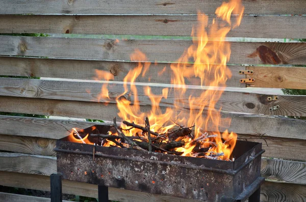 Dry wood for grilling burn with a large flame on the grill, on a background of a wooden fence