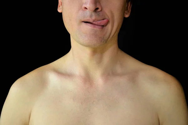 El pecho desnudo de los hombres y la mitad de la cara sobre fondo negro. Un hombre juguetonamente muestra su lengua — Foto de Stock