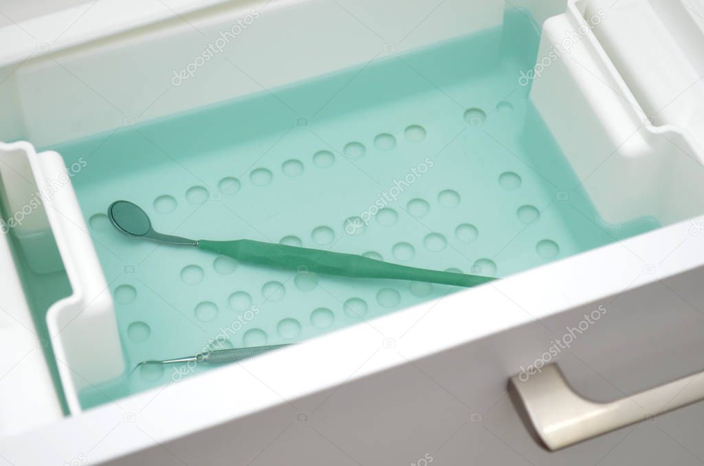 Dental mirror lies in green liquid for sterilization. Instrument is decontaminated