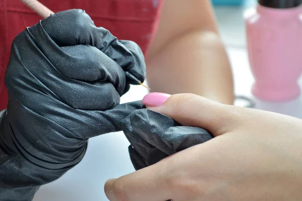 Manicurista en guantes negros aplica esmalte de uñas rosa por pincel —  Fotos de Stock