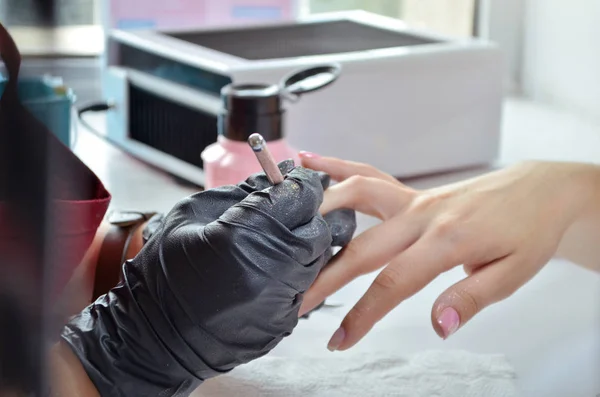 Meester van manicure schildert roze gel Polish op nagels, op de achtergrond van de fles en de droger — Stockfoto