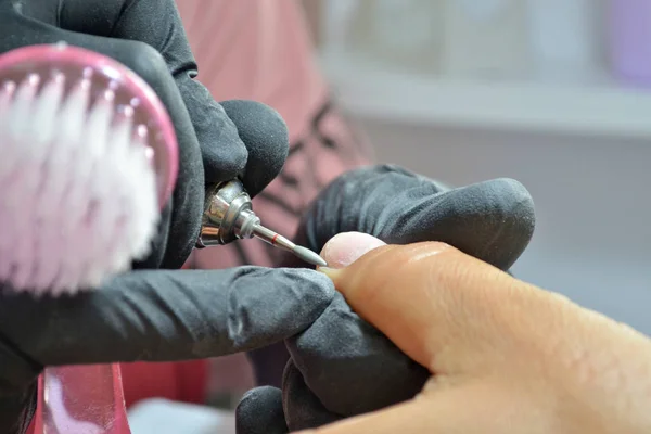 Master of manicure in black gloves and with a brush makes hardware manicure by nail cutter, closeup