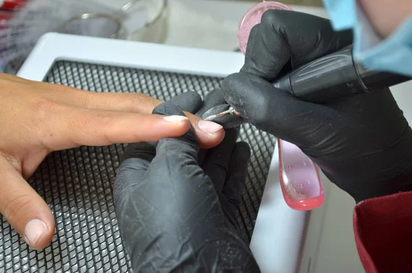 Master of manicure in black gloves and with a brush makes hardware manicure by a nail cutter, top view on dryer