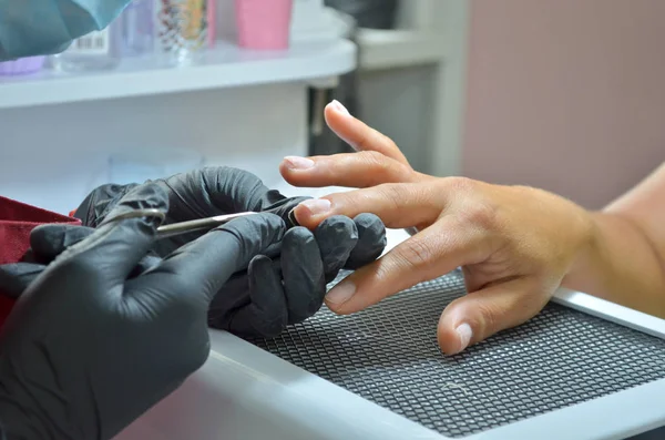 La manicura en guantes negros hace una manicura cortada, recortando la cutícula con una tijera —  Fotos de Stock