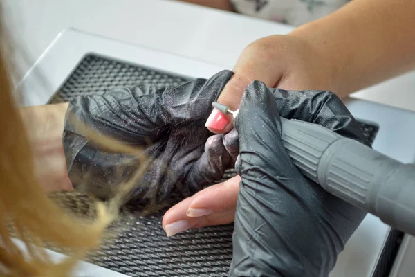 Master of manicure in black gloves removes gel polish with a router
