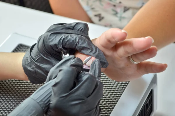 El maestro de la manicura en los guantes negros quita el gel-esmalte con el router bajo la secadora —  Fotos de Stock
