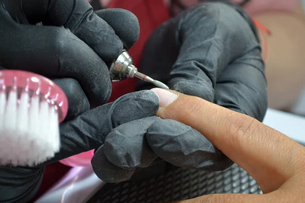Master of manicure in black gloves and with a brush makes hardware manicure by nail cutter