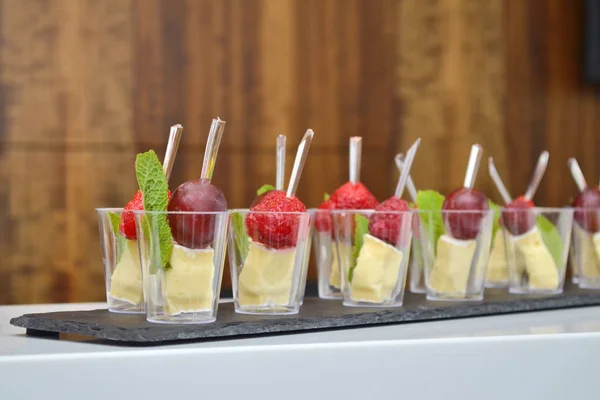 Canapés de frutas e queijo em copos transparentes e espetos de madeira em uma tábua de pedra no banquete — Fotografia de Stock