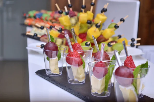 Olika frukt och ost kanapéer i genomskinliga glas och trä spett på ett glas steg stöd på ett bord — Stockfoto