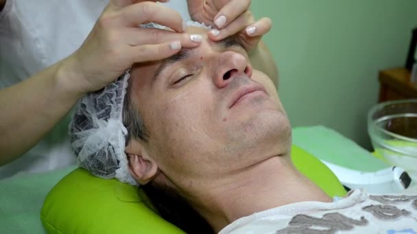 Beautician menerapkan krim di wajah manusia, menerapkan pelembab di sekitar mata — Stok Video