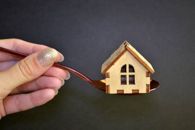 Ahşap sarı oyuncak ev siyah arka plan üzerinde kadın el tarafından düzenlenen mor metal kaşık yatıyor, satın alma kavramı
