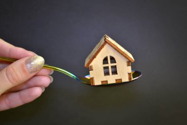 Ahşap sarı oyuncak ev siyah arka plan üzerinde kadın el tarafından düzenlenen gökkuşağı metal kaşık yatıyor, satın alma kavramı
