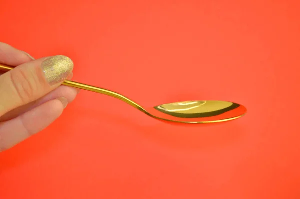 Colher de metal dourado vazia realizada por uma mão feminina com manicure em fundo de coral, com copyspace — Fotografia de Stock