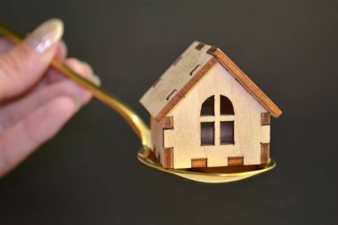 Ahşap sarı oyuncak ev siyah arka plan üzerinde kadın el tarafından düzenlenen renkli metal kaşık yatıyor, satış kavramı