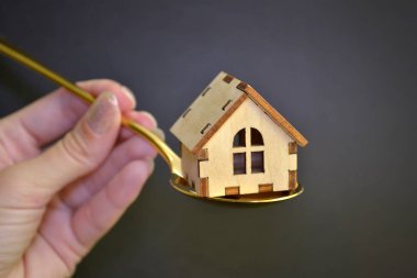Ahşap sarı oyuncak ev siyah arka plan üzerinde bir kadın el tarafından düzenlenen altın bir metal kaşık yatıyor, satış kavramı
