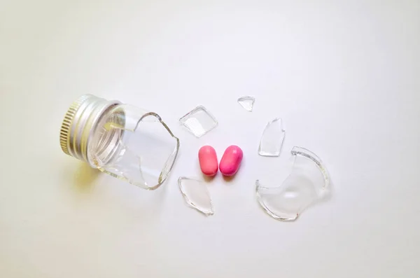 A broken glass bottle with a metal cap, two pink heart-shaped tablets fell out of it, on a white background — Stock Photo, Image