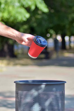 Erkek el çöp konteynerkahve için kırmızı bir kağıt fincan attı, uçuş fincan, yeşil ağaçların arka plan, dikey