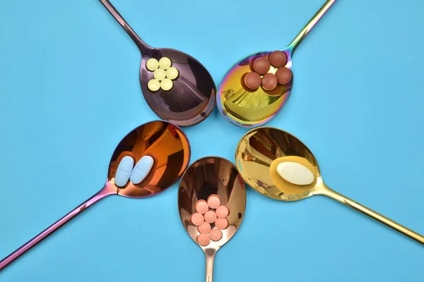 Fünf verschiedene Pillen in fünf mehrfarbigen Metalllöffeln in Blütenform auf blauem Hintergrund — Stockfoto