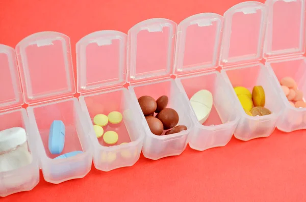 Plastic daily organizer for pills, box with different pills on pink background with copyspace, top view