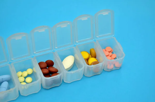 Plastic daily organizer for pills, box with different pills on blue background with copyspace, top view — Stok fotoğraf