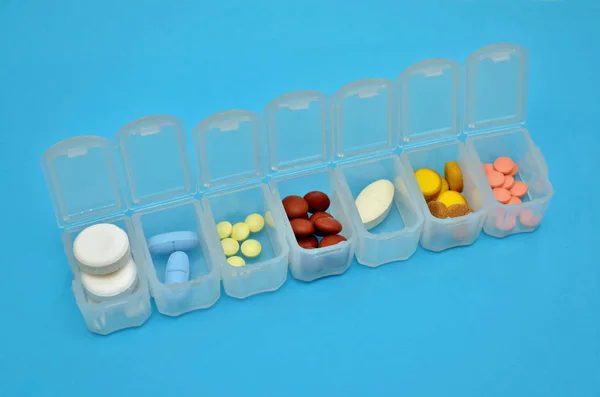 Plastic daily organizer for pills with different pills on blue background with copyspace, top view — Stok fotoğraf