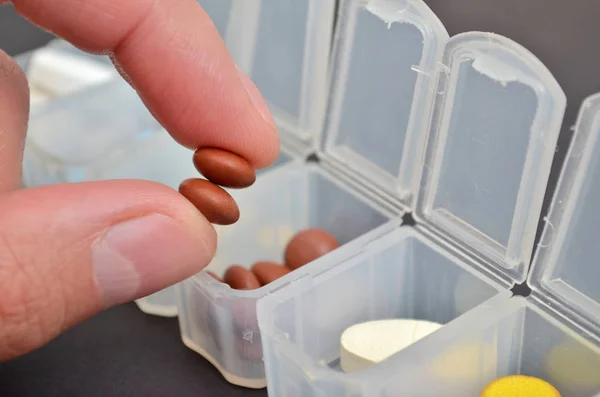 Man hand takes brown pills from plastic organizer for pills on a black background with copyspace