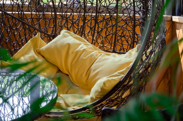 Room decor, cocoon chair with yellow pillows, glass table, plant and wooden wall