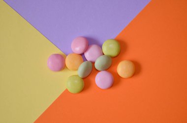 Yuvarlak renkli şekerler üç renk, sarı, mavi ve turuncu, geometrik arka plan, üst görünüm demet yalan