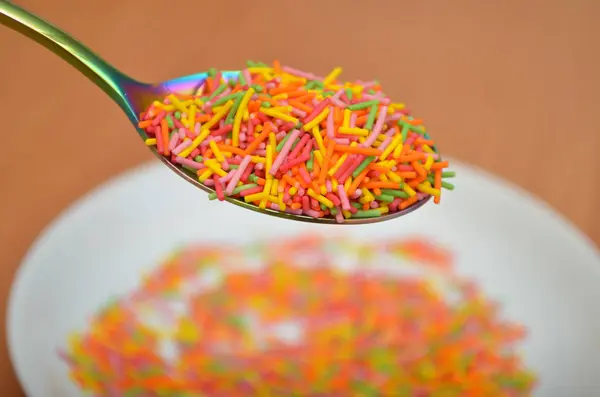 Long baking topping, sprinkle in a white saucer with rainbow spoon under it, on a wooden table Royalty Free Stock Photos