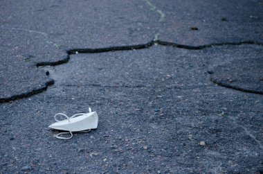 Beyaz tıbbi maske, şehirdeki kirli gri asfalt üzerindeki çöp gibi duruyor. Karantina yorgunluğu ve koronavirüs salgınının sembolü.