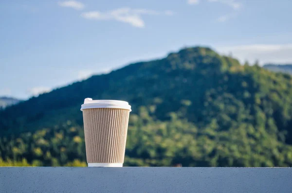 Brown disposable cup of coffee on background of green carpathian mountains and blue sky